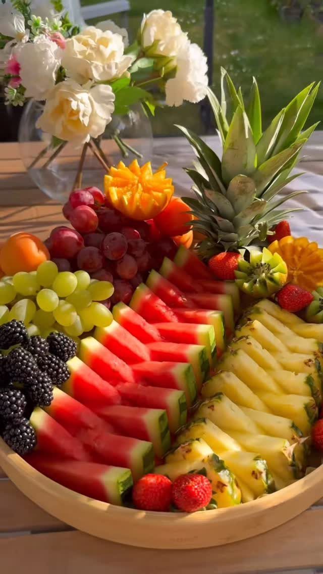 Wooden bowl of sliced tropical fruits and berries next to white flowers.
