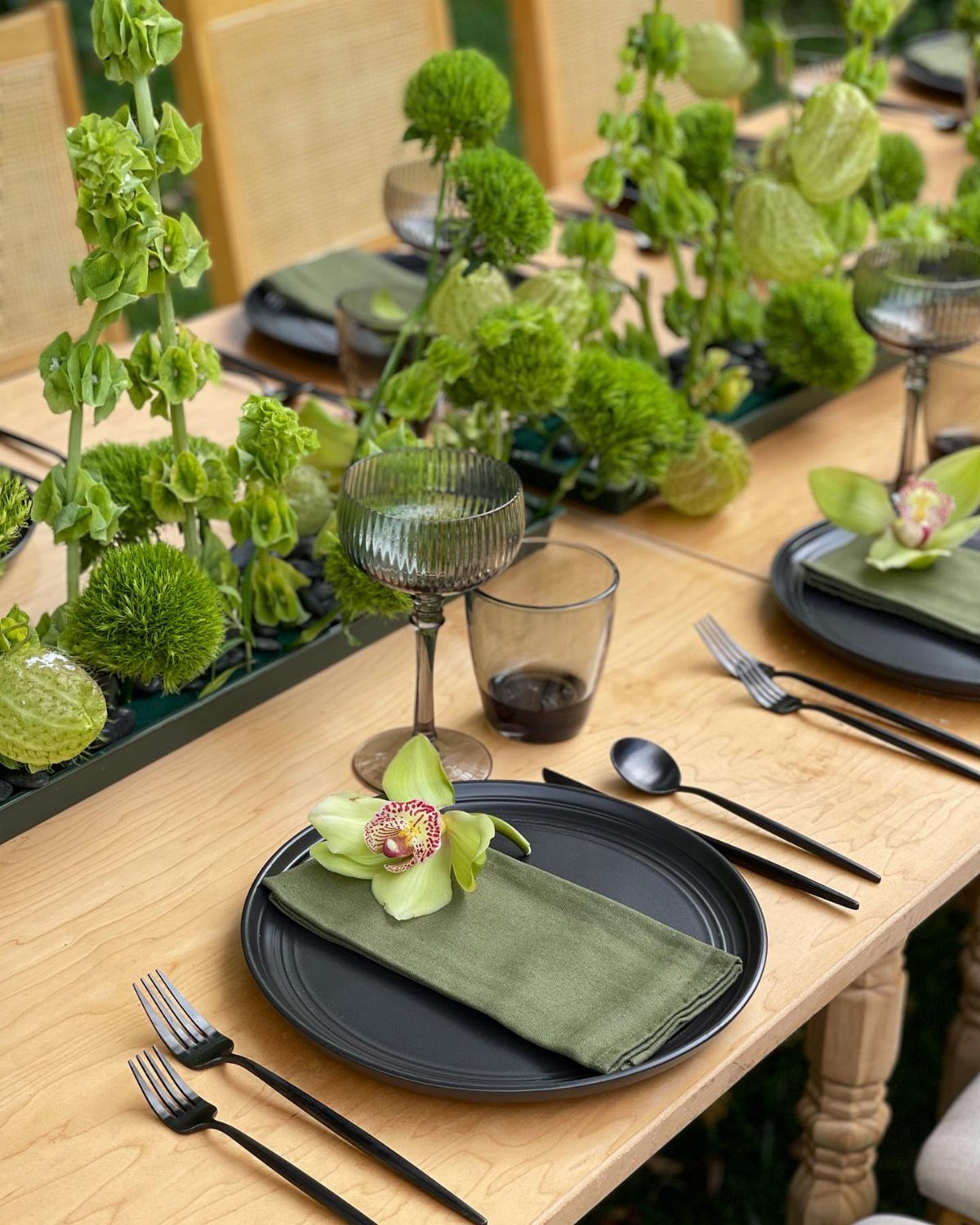 Greenery centerpieces in a black planter on a wooden table with black plates.