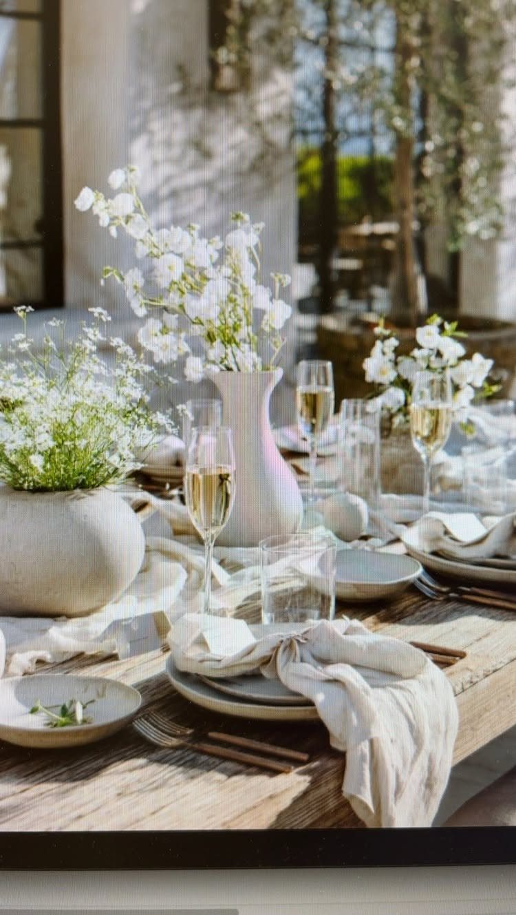 Rustic wooden table set with white linens, white flowers, and glasses of wine.