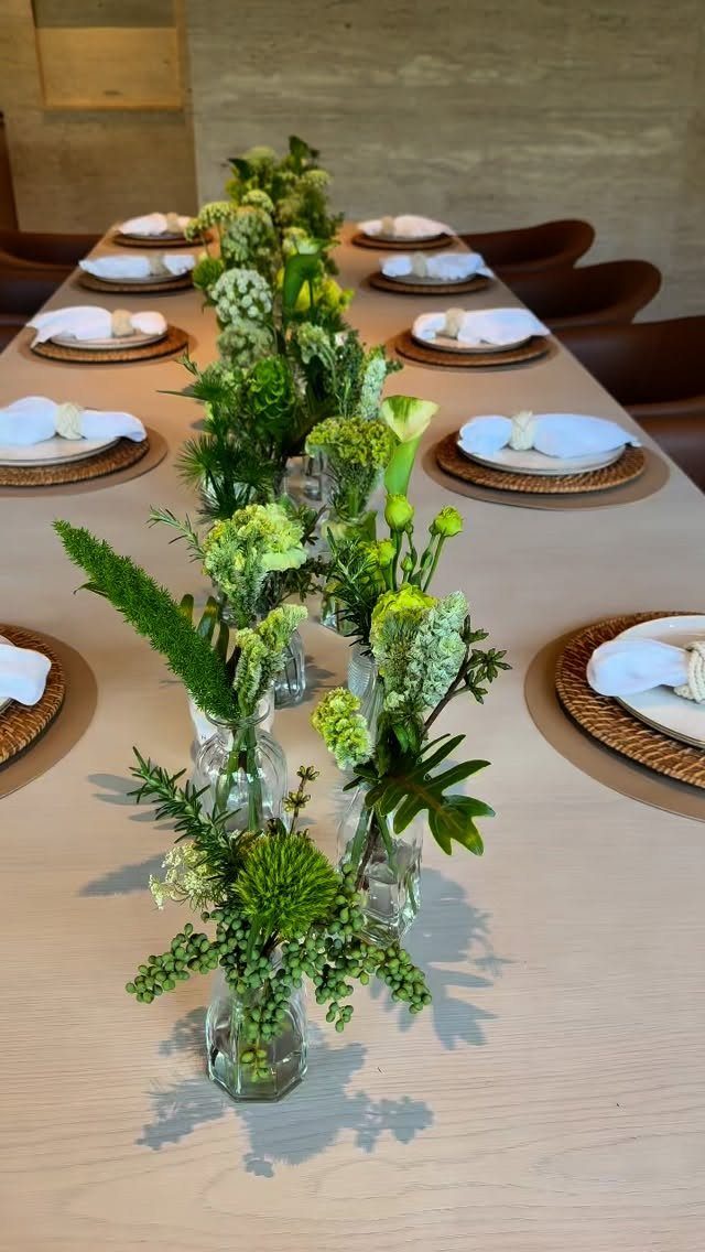 Green floral arrangements in small glass vases lining a set wooden dining table
