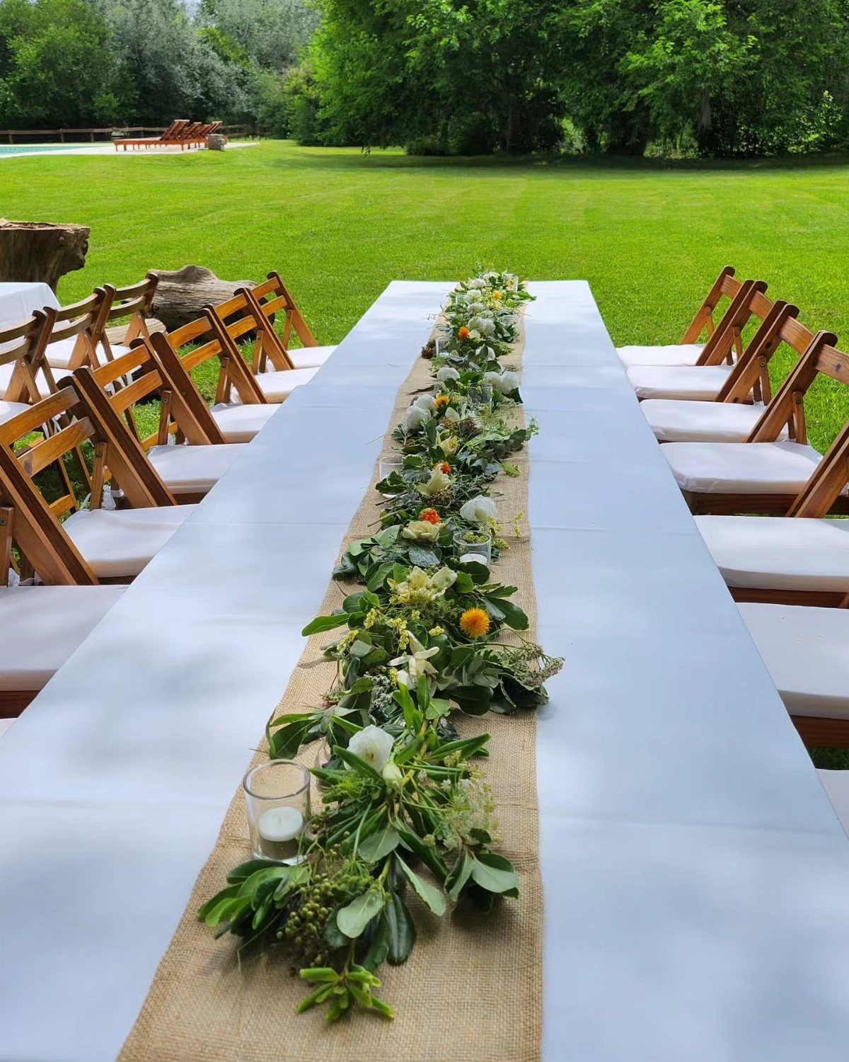 Eucalyptus branch garland with white flowers and candles on a white outdoor table.