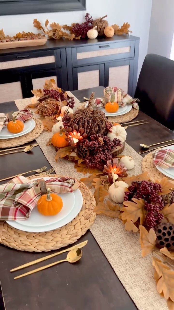 Autumn dinner table centerpiece with pumpkins, fall leaves, and berries on burlap runner.