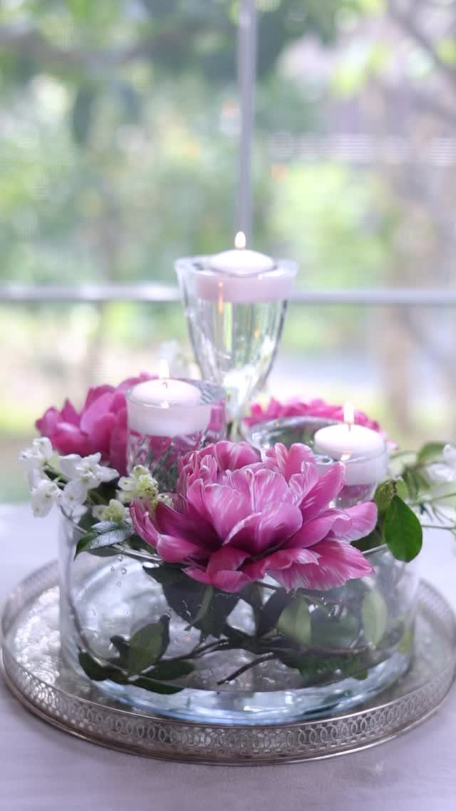 Glass bowl with pink peonies and floating candles on a silver tray