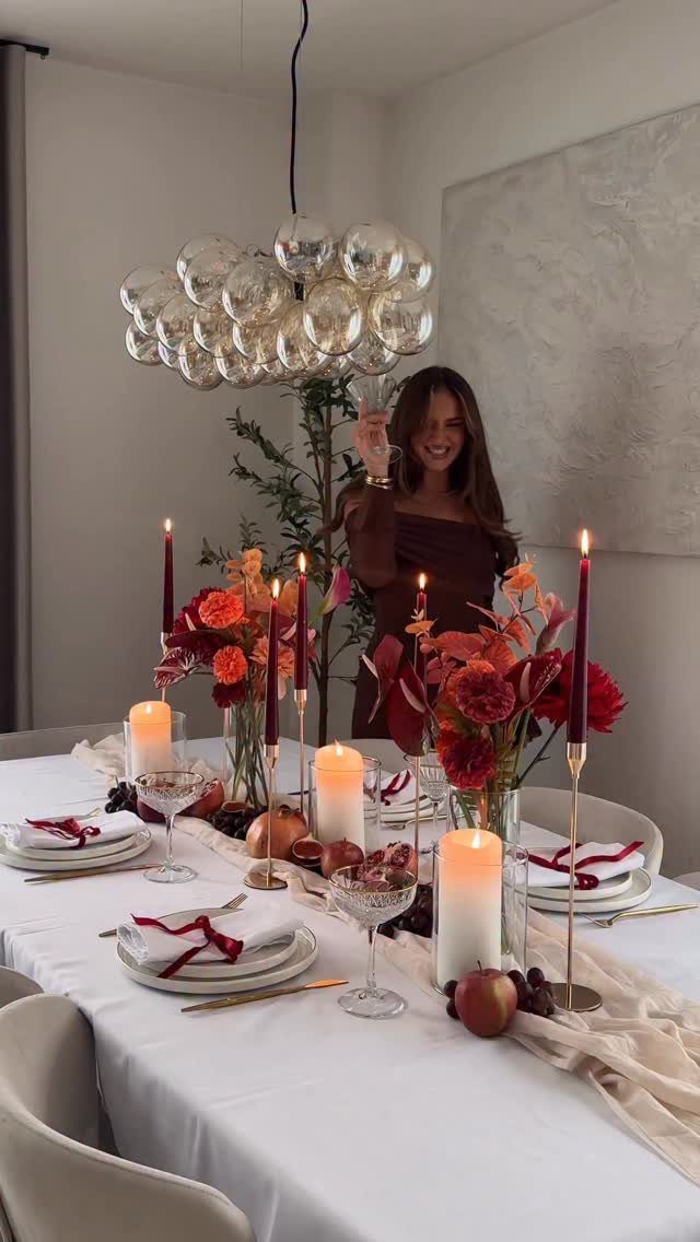 Woman standing behind a dinner table set with red flowers and candles.