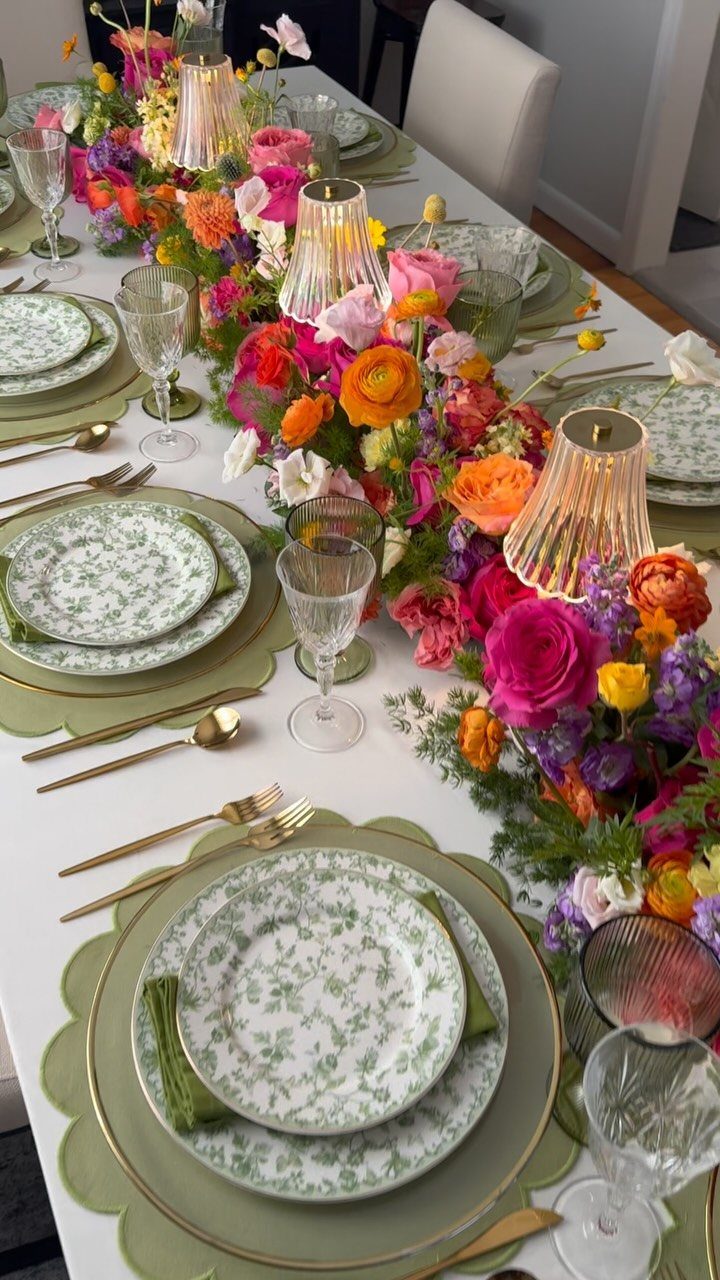 Floral dinner table setting with green plates, gold cutlery, and colorful flower centerpiece.