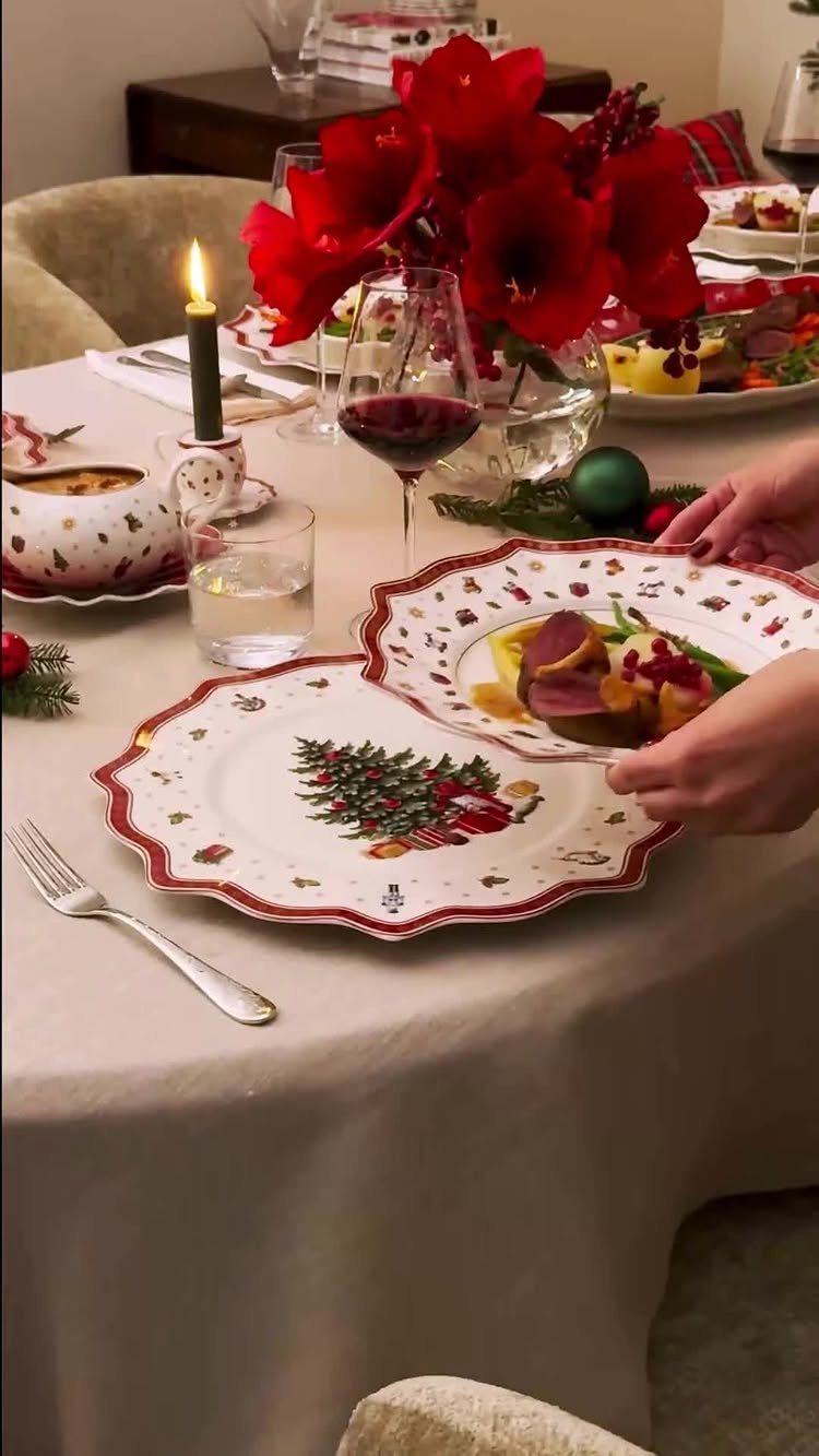 Holiday dinner table setting with red flowers, Christmas plates, and a lit candle.