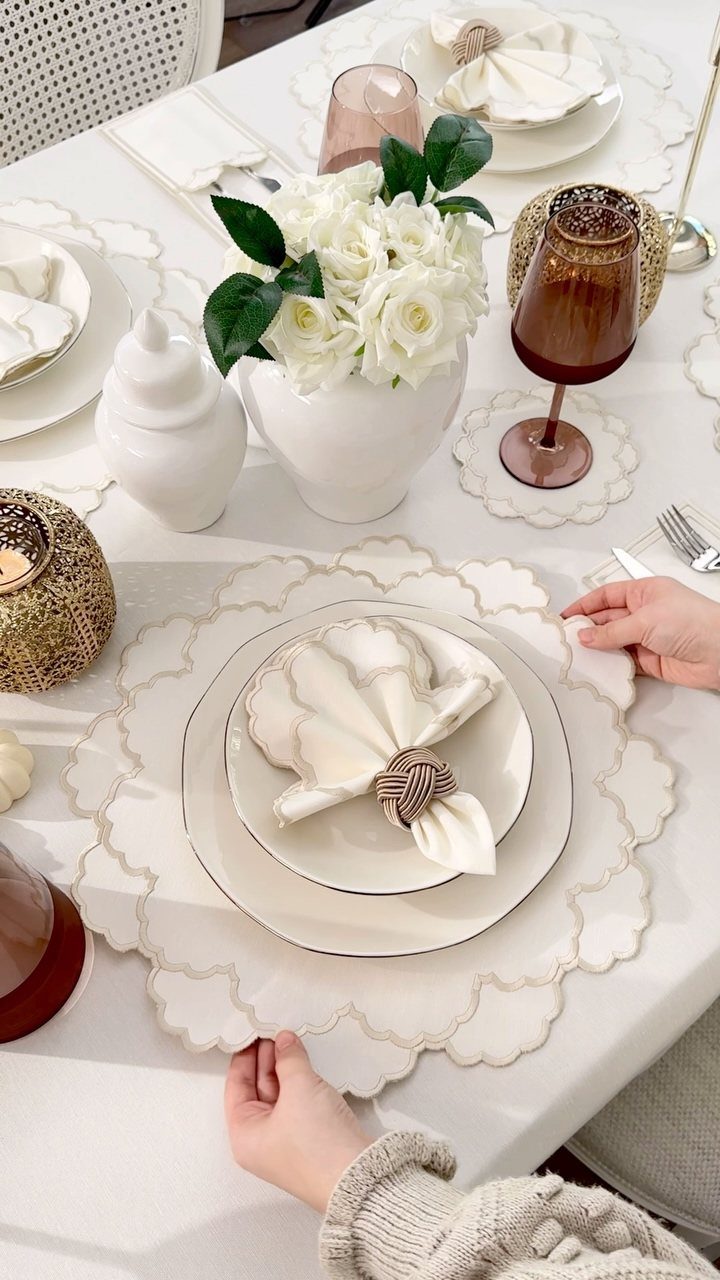 Scalloped cream placemats under white porcelain plates with white roses and amber glassware.