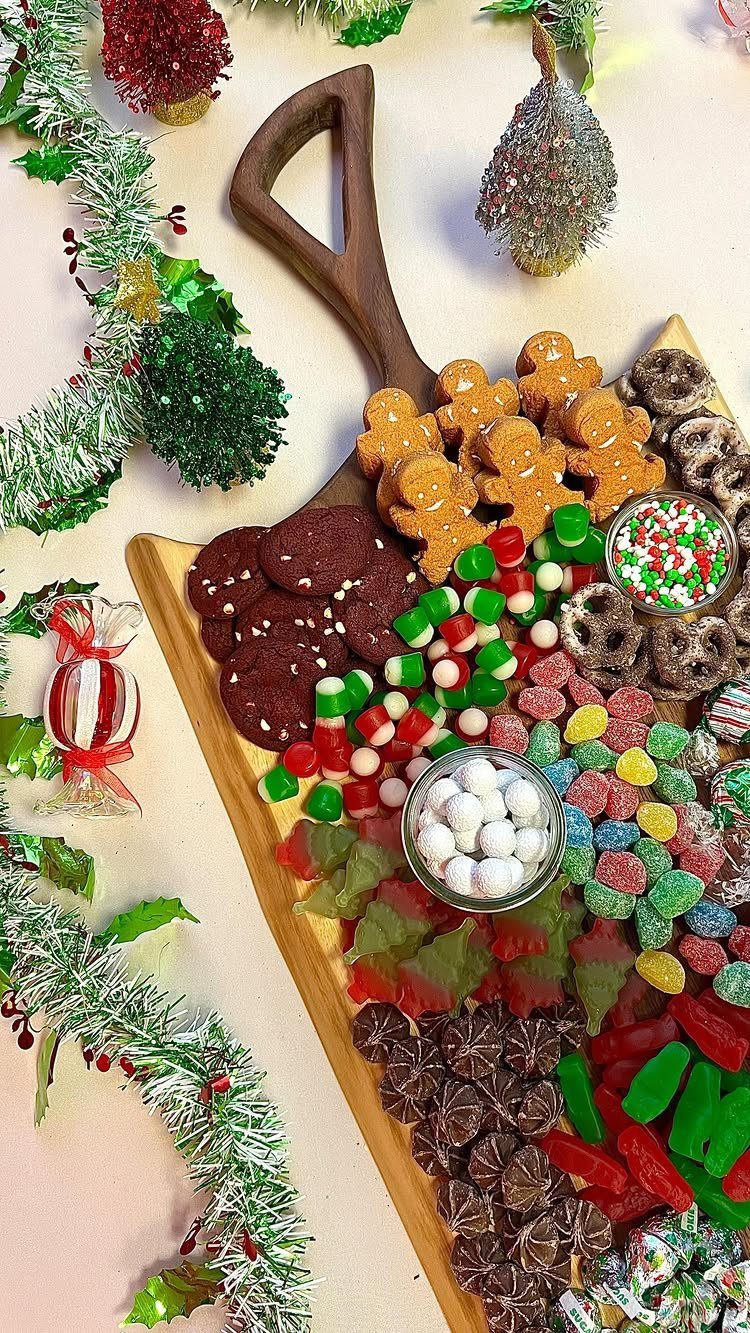 Wooden grazing board filled with gingerbread men, chocolate cookies, and colorful Christmas candies.
