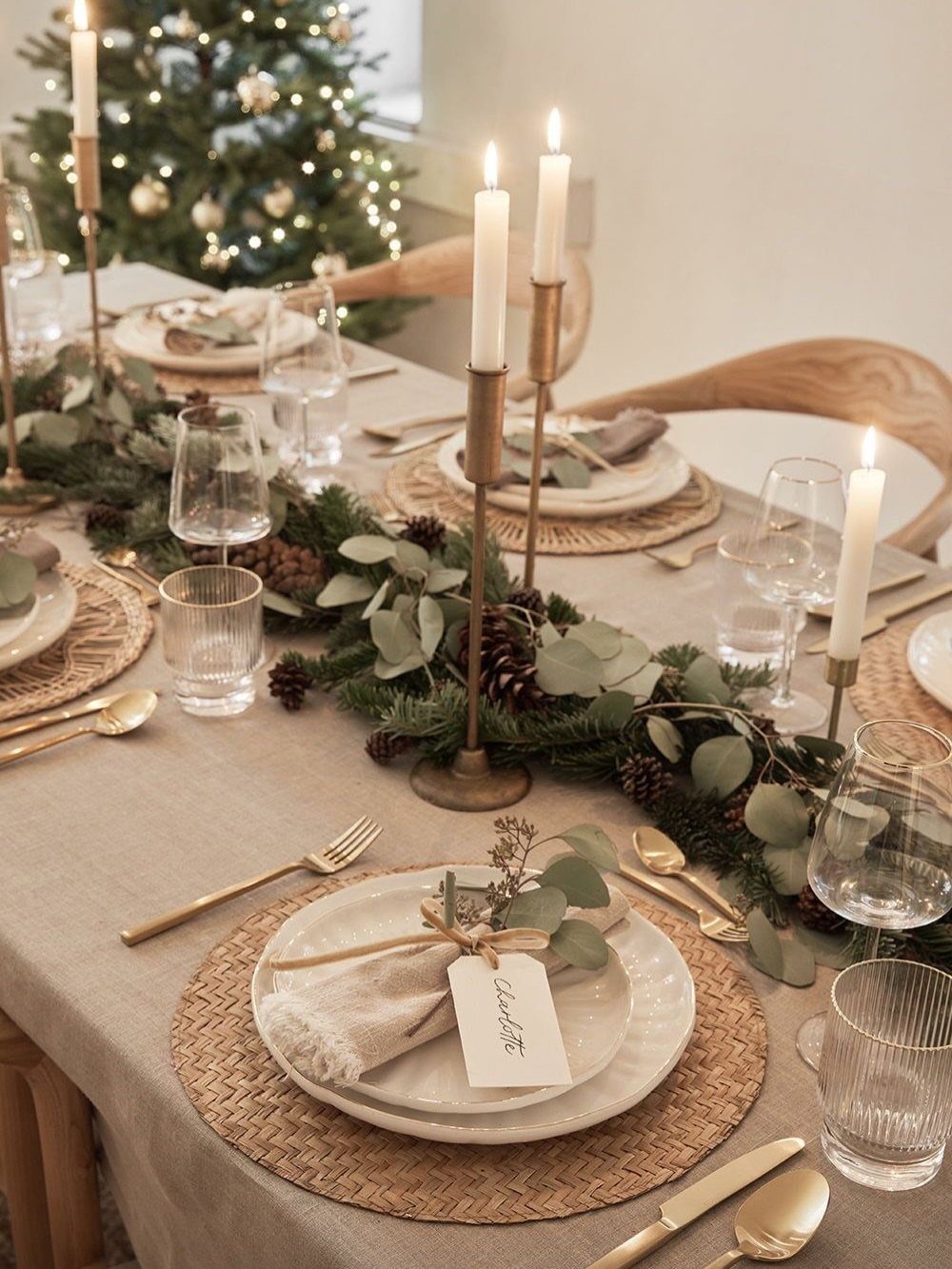Festive dining table with greenery garland, white candles, and woven charger plates.