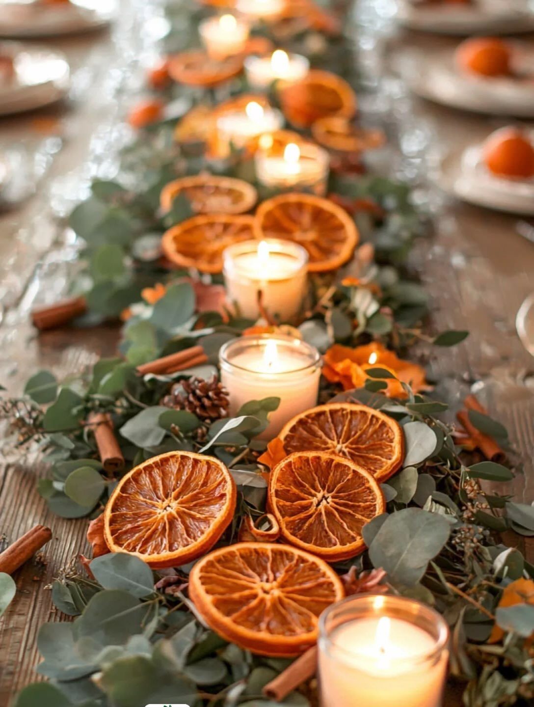 Festive table runner with dried orange slices, eucalyptus leaves, and glowing white candles.