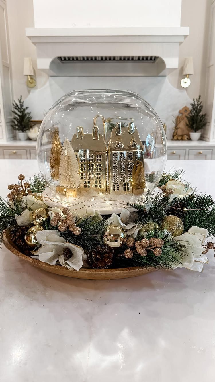 Gold miniature village inside a glass dome surrounded by festive holiday greenery