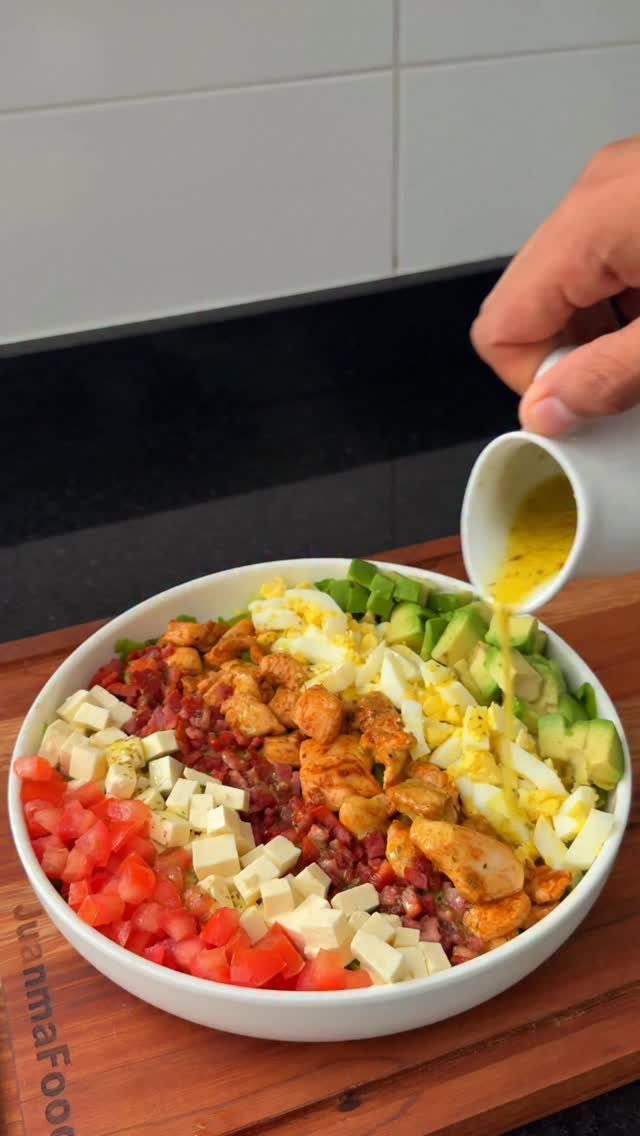 Cobb salad in a white bowl with dressing being poured over the top.