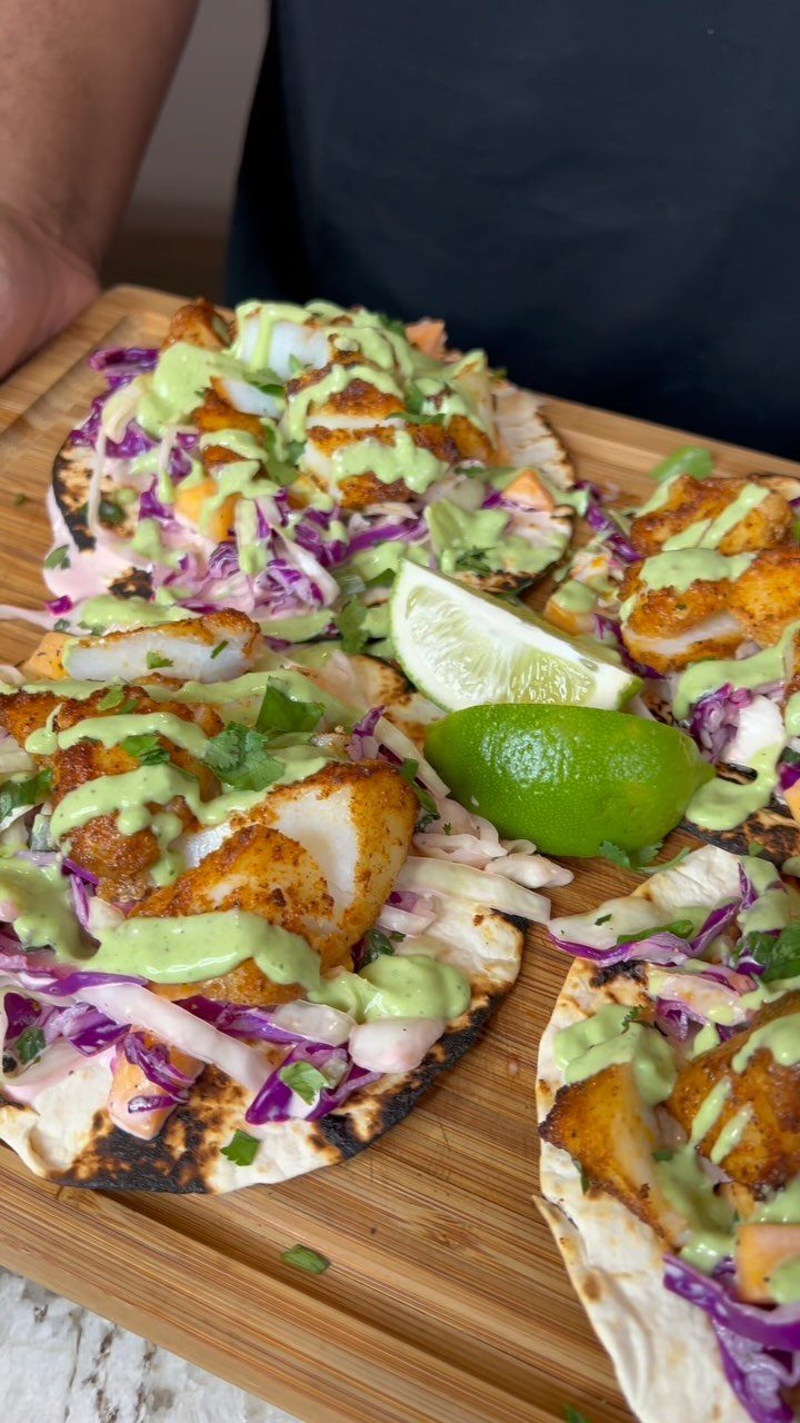 Fish tacos with purple cabbage slaw and green sauce on a wooden board.