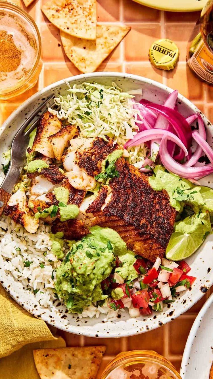 Grilled seasoned fish bowl with rice, guacamole, cabbage slaw, and pickled onions.