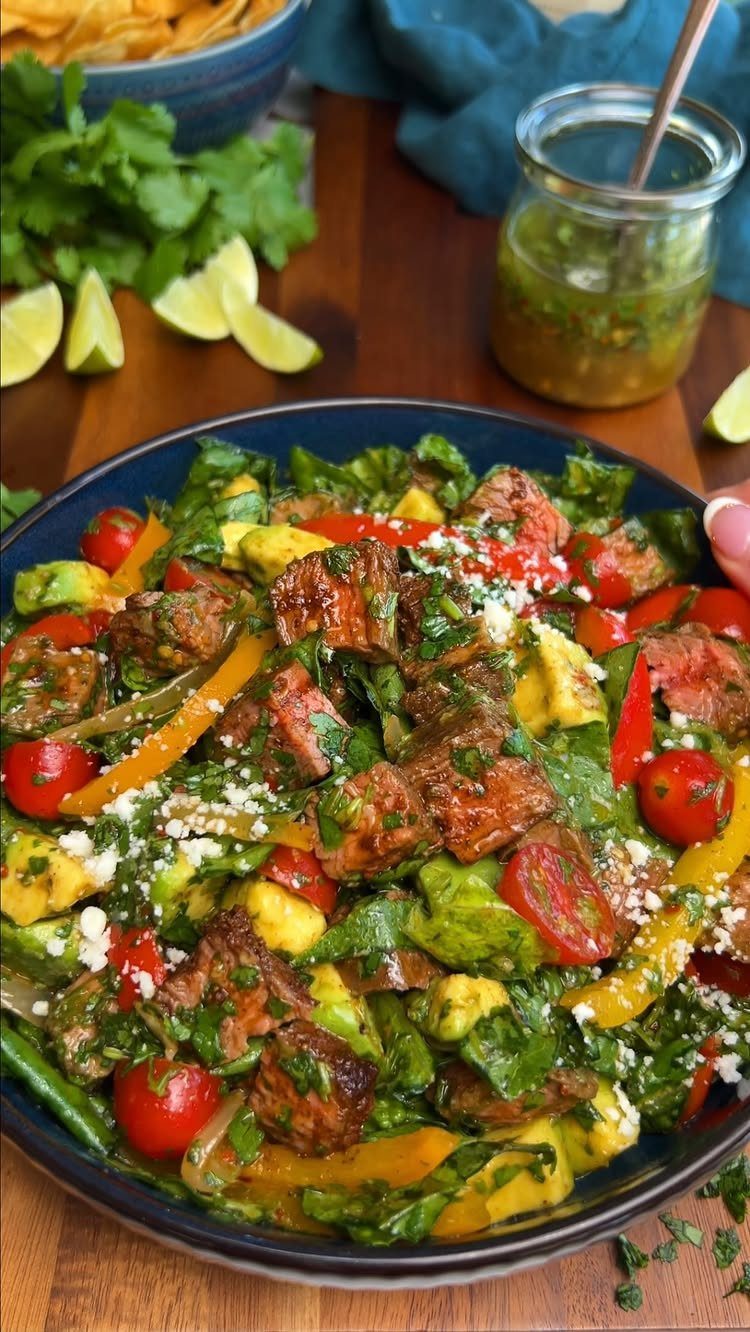 Grilled meat salad with cherry tomatoes, avocado, and feta in a blue bowl.
