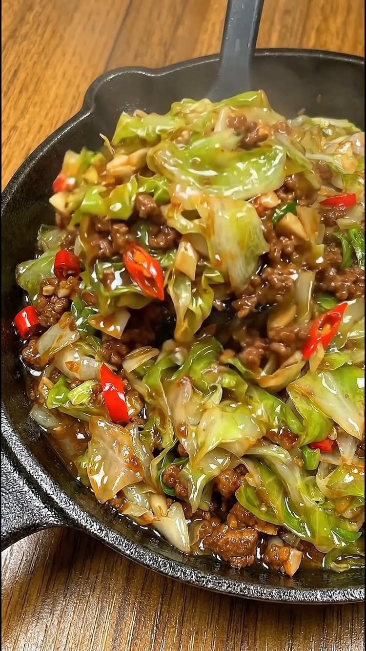Ground beef and cabbage stir-fry with red chilies in a cast iron skillet.