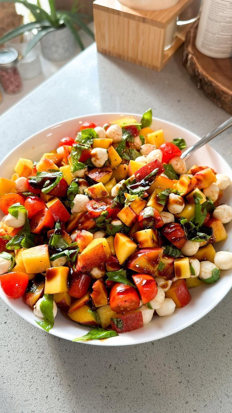 Tomato peach caprese salad with mozzarella and basil in a white bowl.