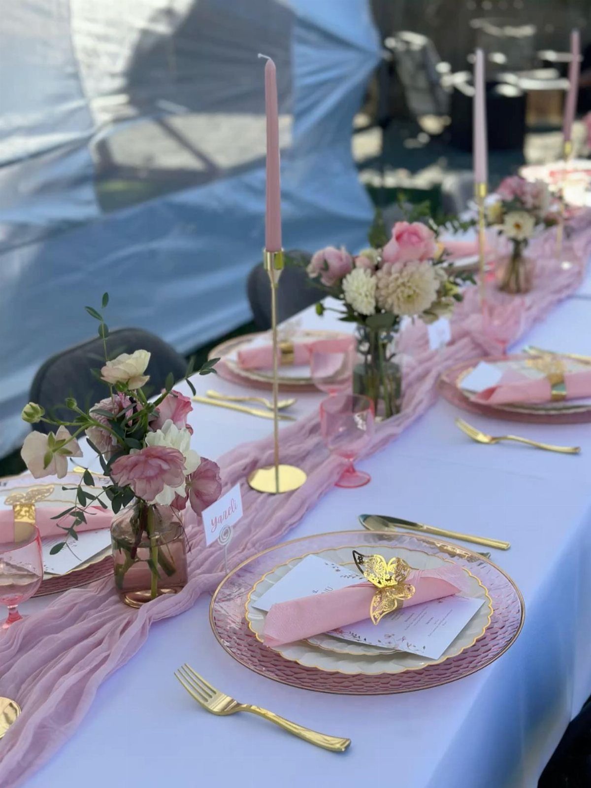 Pink and gold table setting with floral centerpieces and tall pink taper candles.
