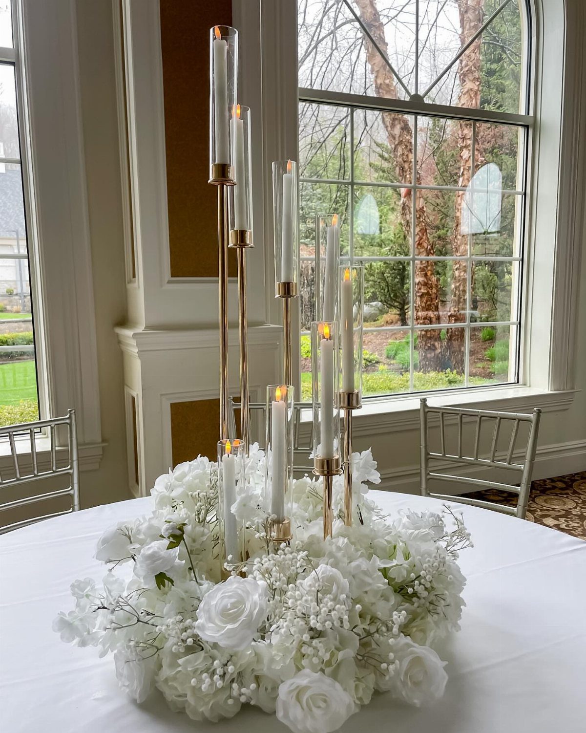 White floral centerpiece with tall gold candle holders on a white round table.