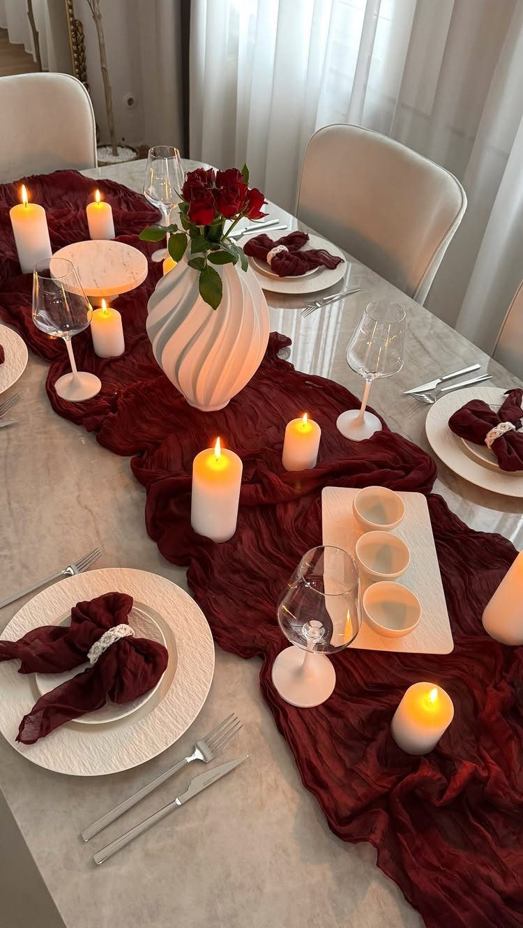 Dining table with burgundy runner, white plates, red roses, and white pillar candles.