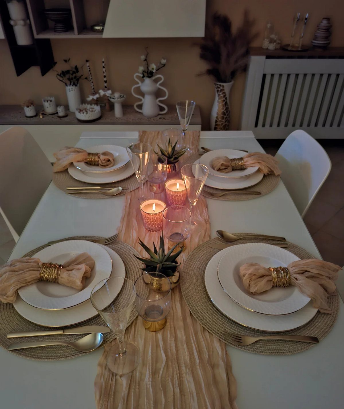 Beige and white table setting with gold accents, candles, and small succulents.