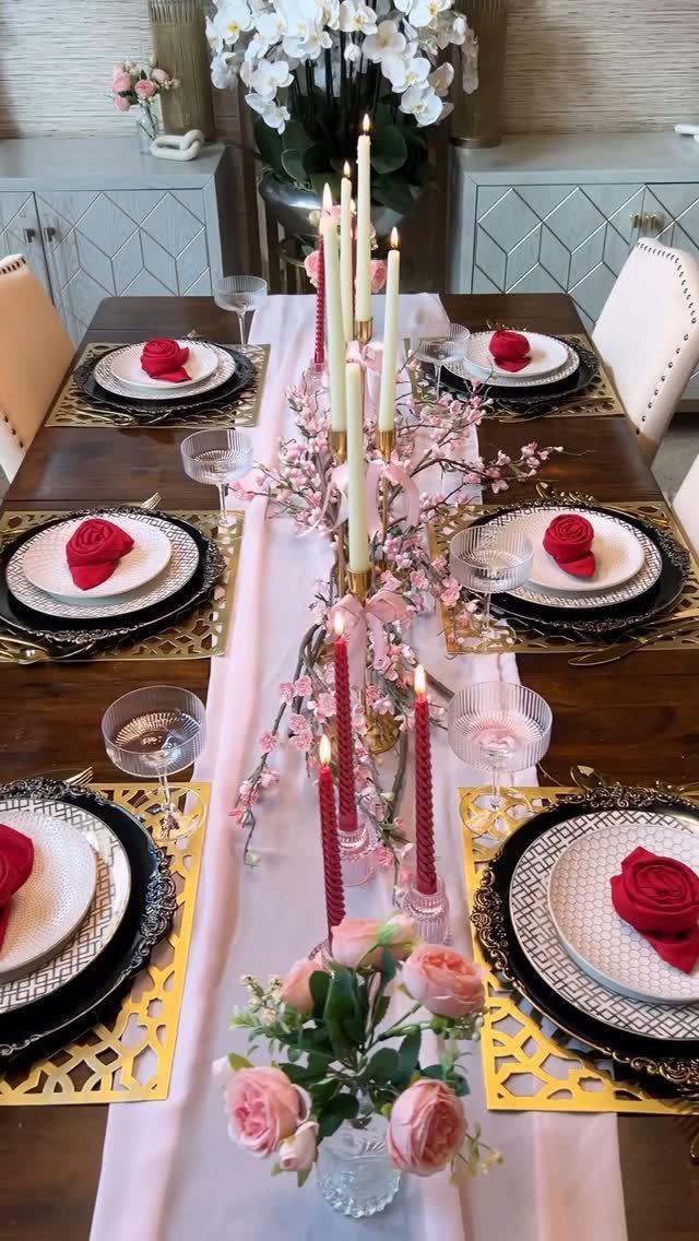 Elegant dining table with red rose napkins, gold placemats, and pink floral centerpieces.