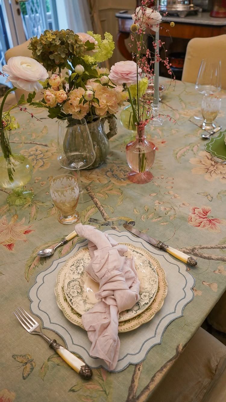 Formal table setting with floral tablecloth, ornate plates, and fresh flower arrangements.