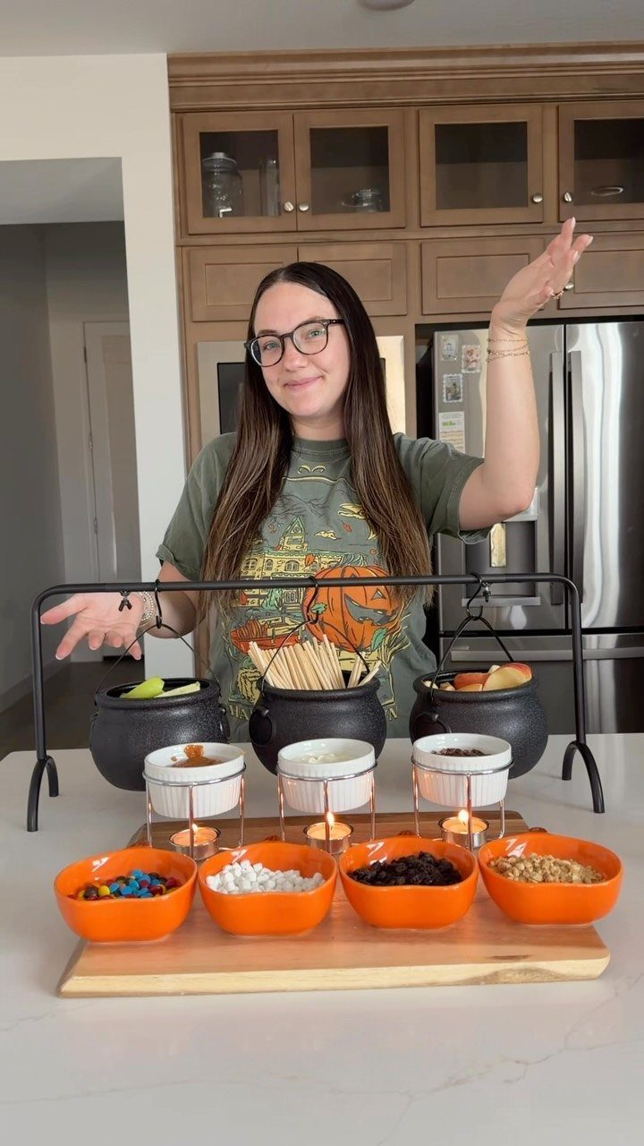 Woman presenting a caramel apple bar with cauldrons, fondue pots, and candy bowls.