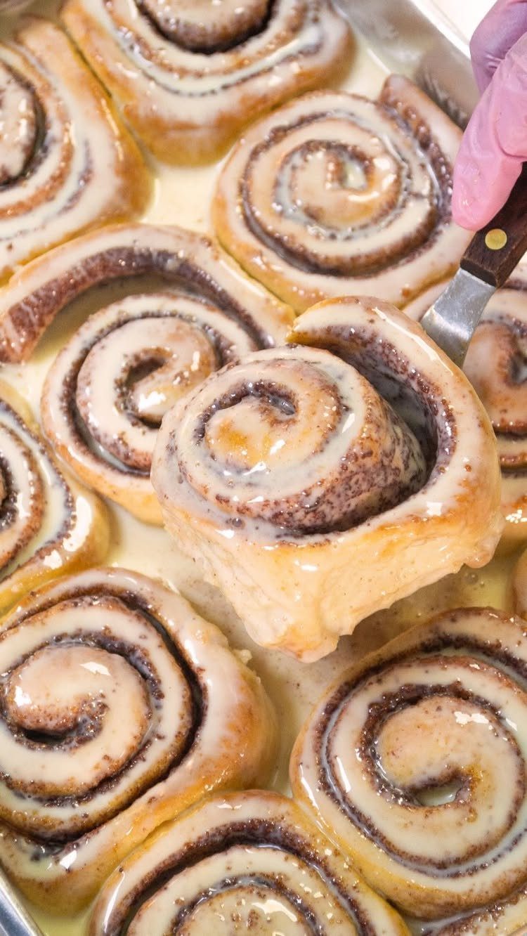 Glazed cinnamon rolls in a baking pan with one being lifted by a spatula.