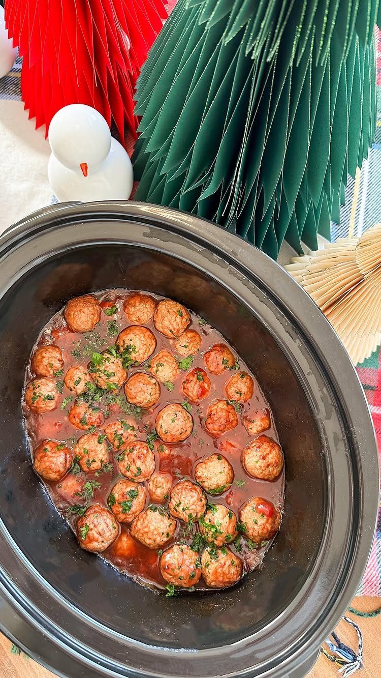 Meatballs in a reddish sauce with parsley in a black slow cooker.