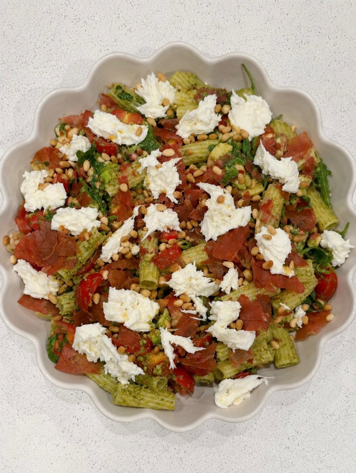 Penne pasta salad with pesto, tomatoes, cured meats, and fresh mozzarella in a bowl.