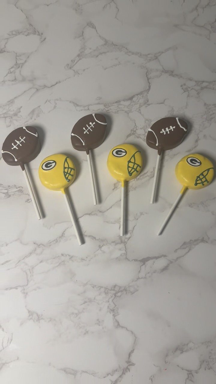 Football cake pops in brown and yellow shapes on a white marble background.