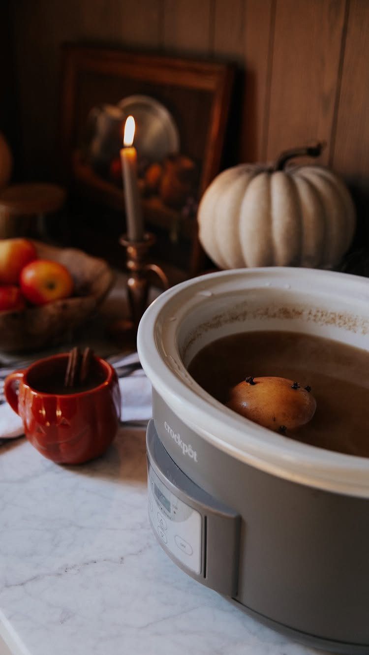 Hot apple cider in a slow cooker and red mug with autumn decorations.