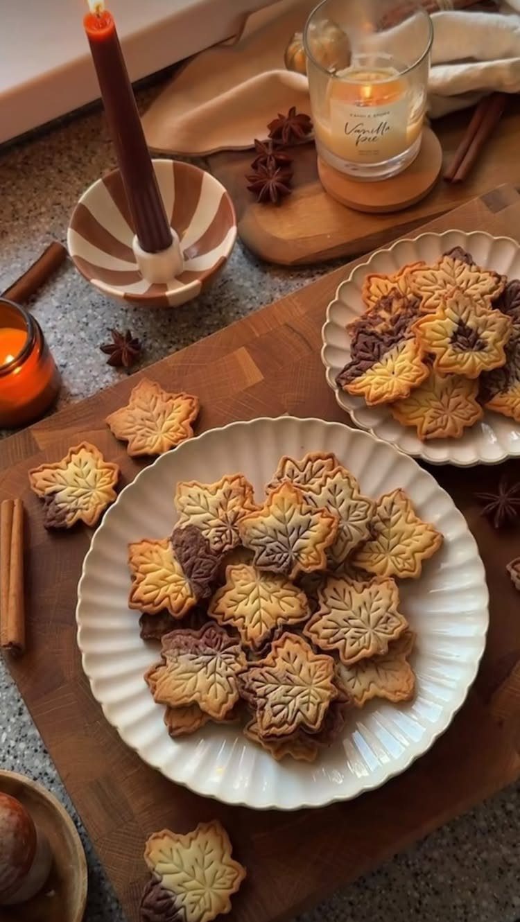 Maple leaf shaped cookies with icing on white plates and a wooden board.
