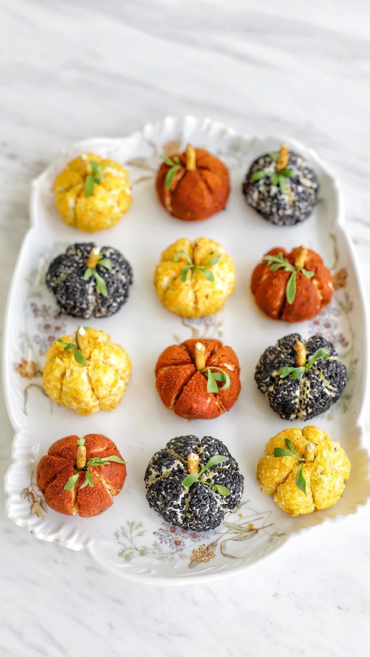 Pumpkin-shaped cheese balls in yellow, orange, and black on a white platter.