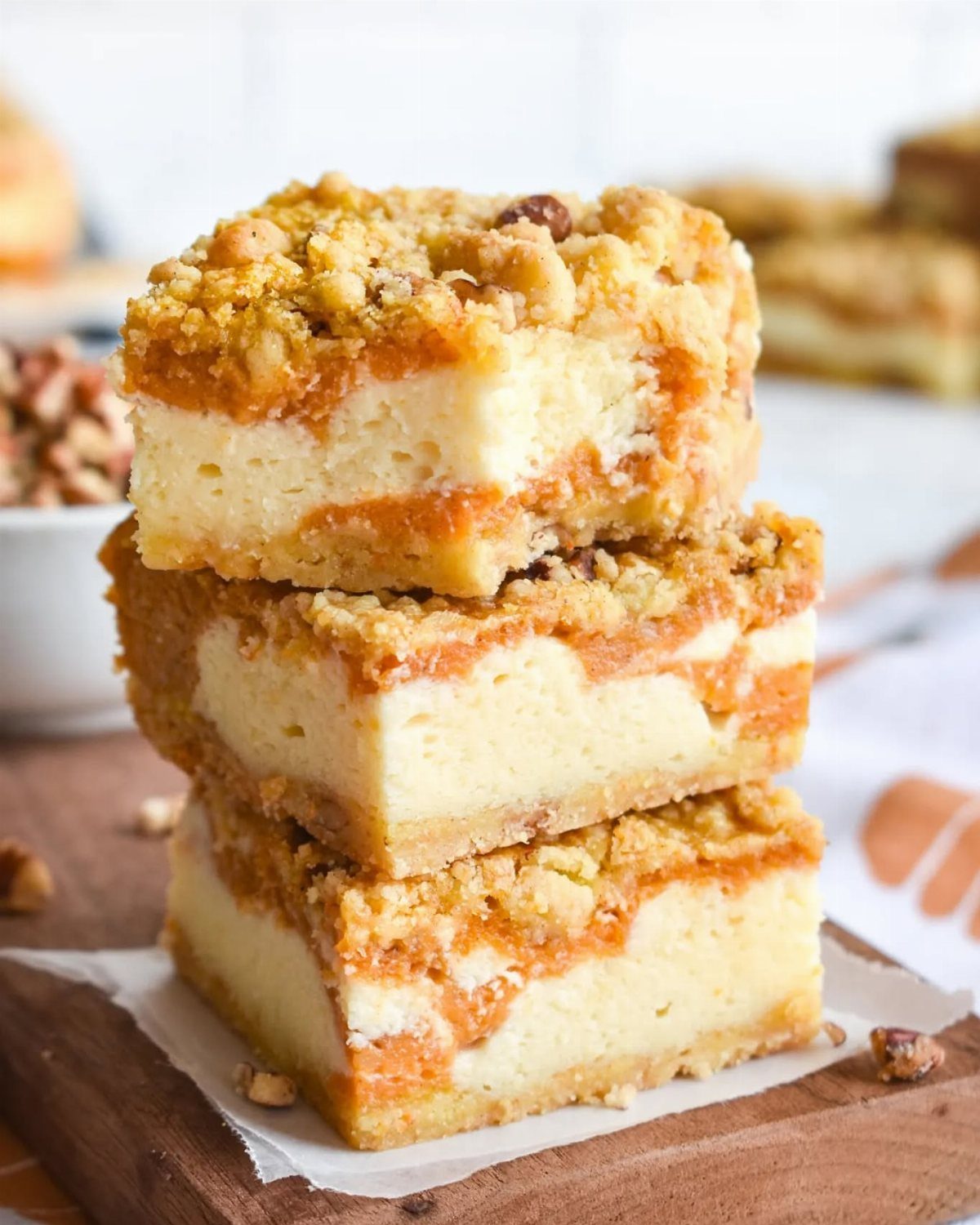 Stacked pumpkin cheesecake bars with a crumbly topping on a wooden board.