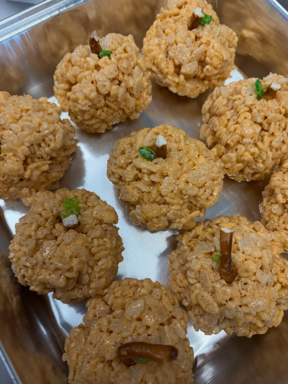 Pumpkin-shaped puffed rice cereal treats with pretzel stems in a metal pan.