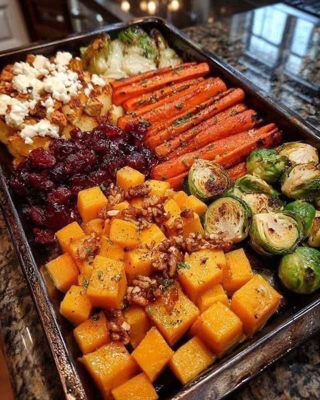 Roasted autumn vegetables including squash, brussels sprouts, and carrots on a baking sheet.
