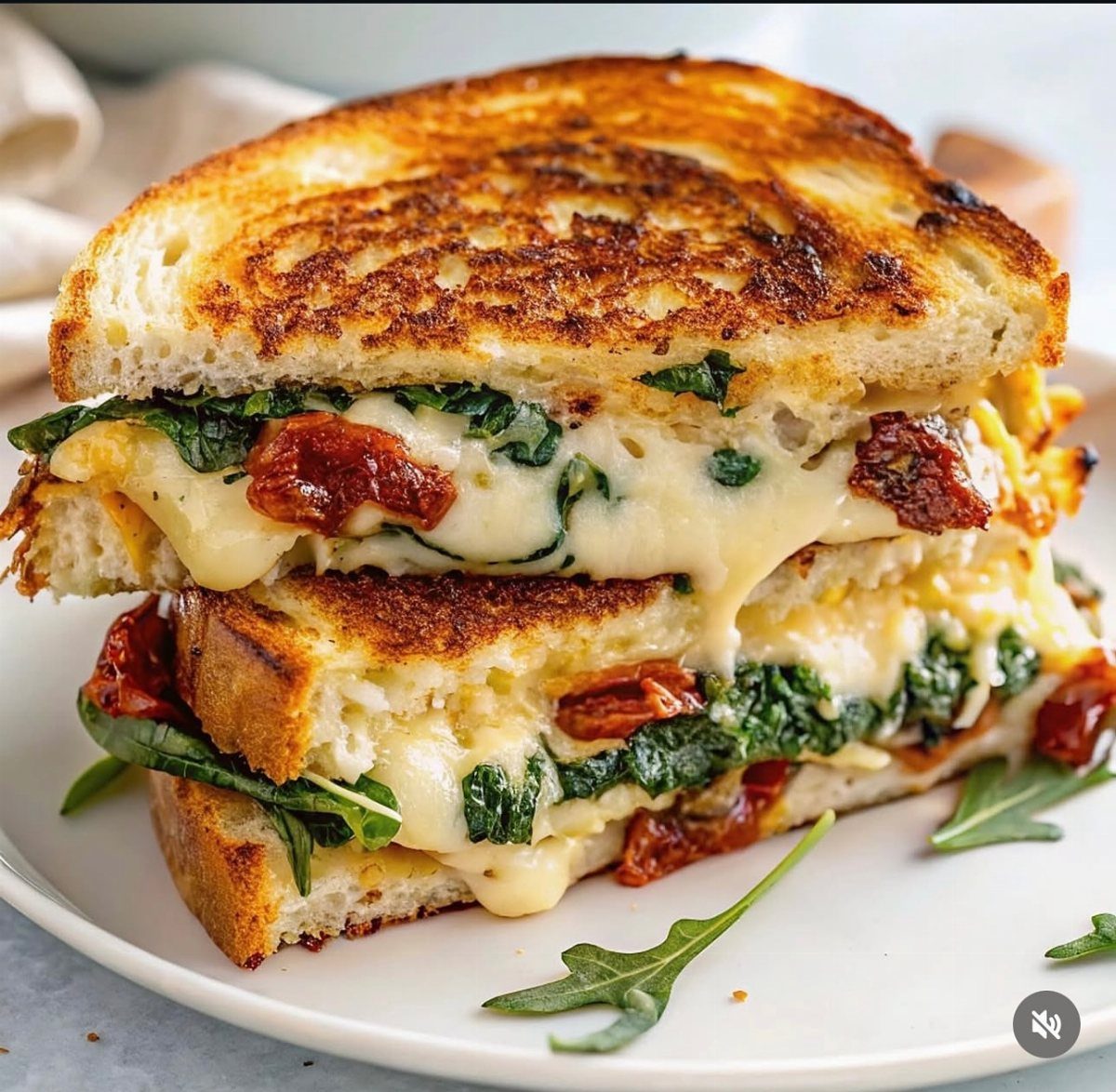 Grilled cheese sandwich with melted cheese, spinach, and sun-dried tomatoes on a plate.