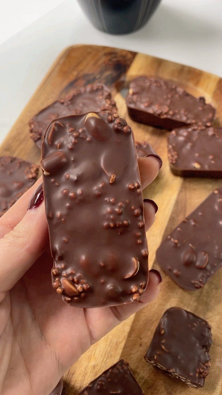 Chocolate nut bars on a wooden board, one held by a hand.
