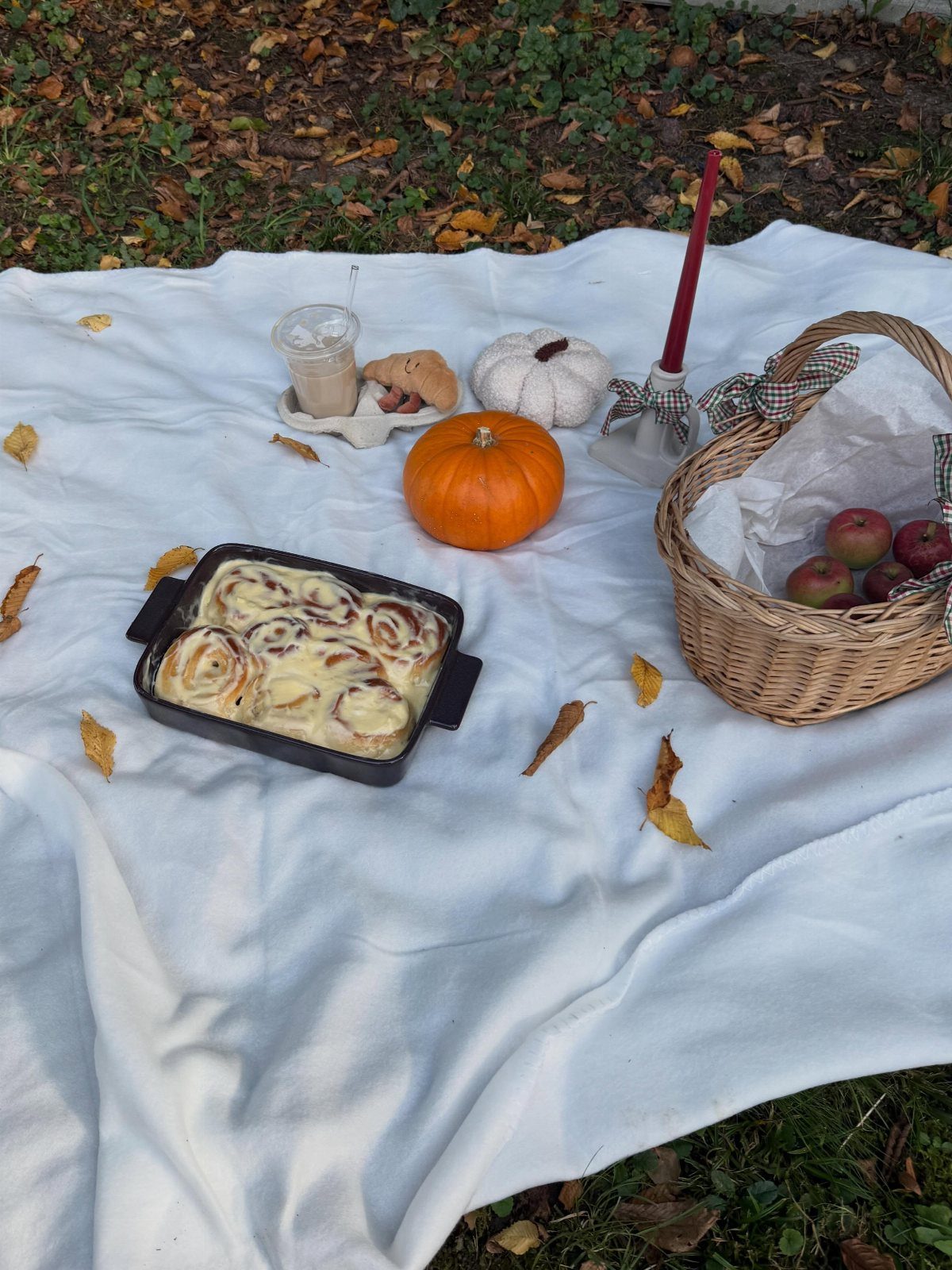 Glazed cinnamon rolls in a black pan on a white autumn picnic blanket.