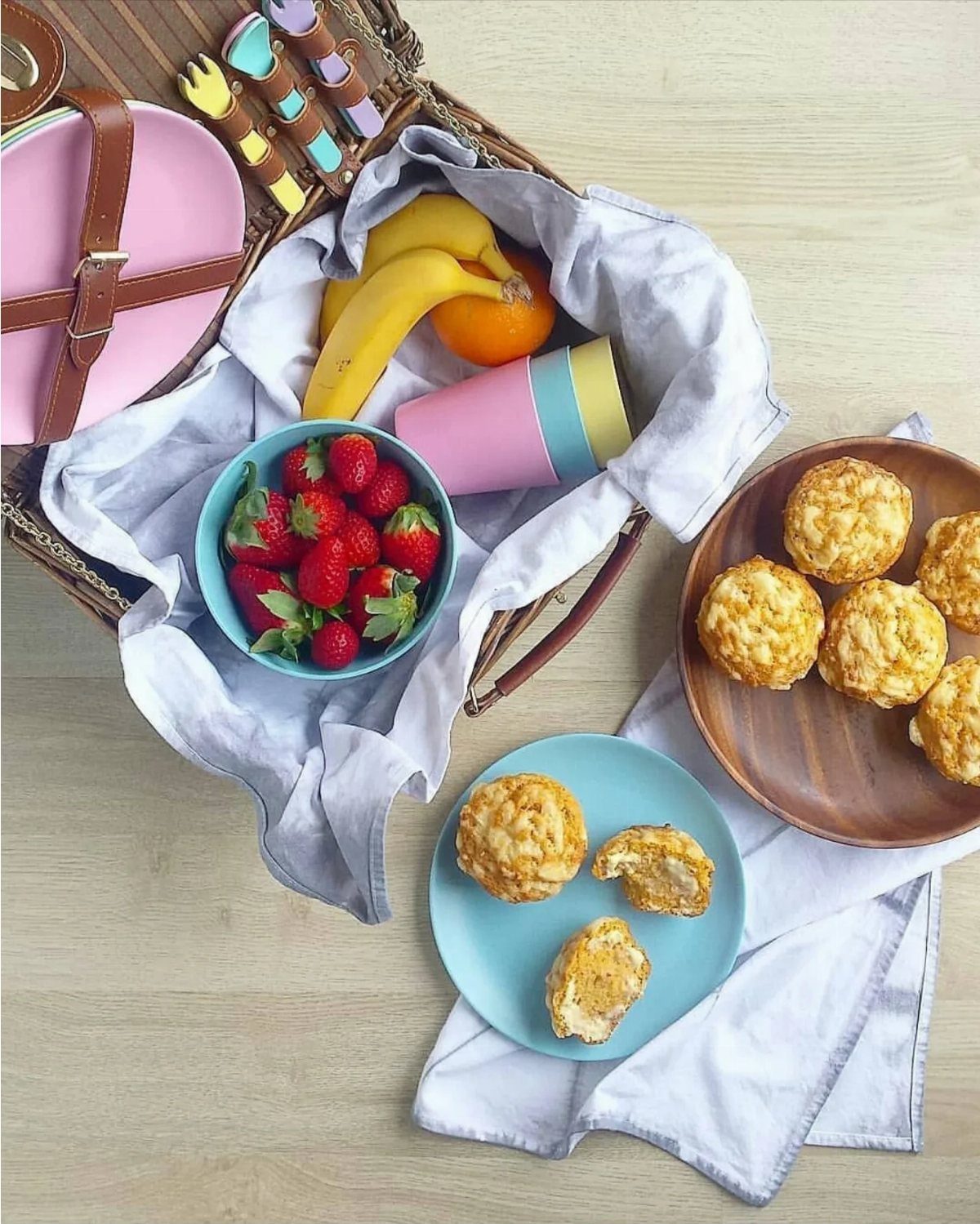 Picnic basket with fresh fruit and golden-brown cheese scones on a wooden table.