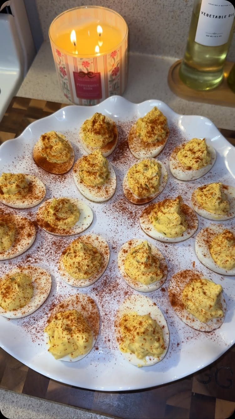 Deviled eggs with creamy yellow filling and paprika on a white scalloped platter.