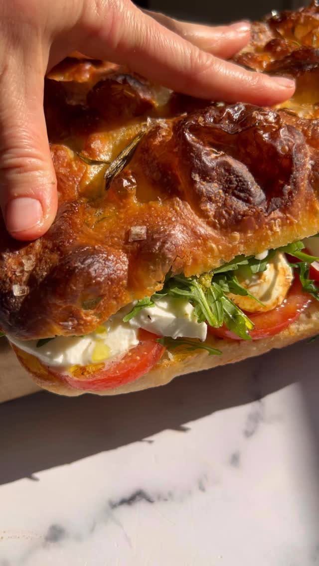 Toasted focaccia sandwich with mozzarella, tomato, and arugula held by a hand.