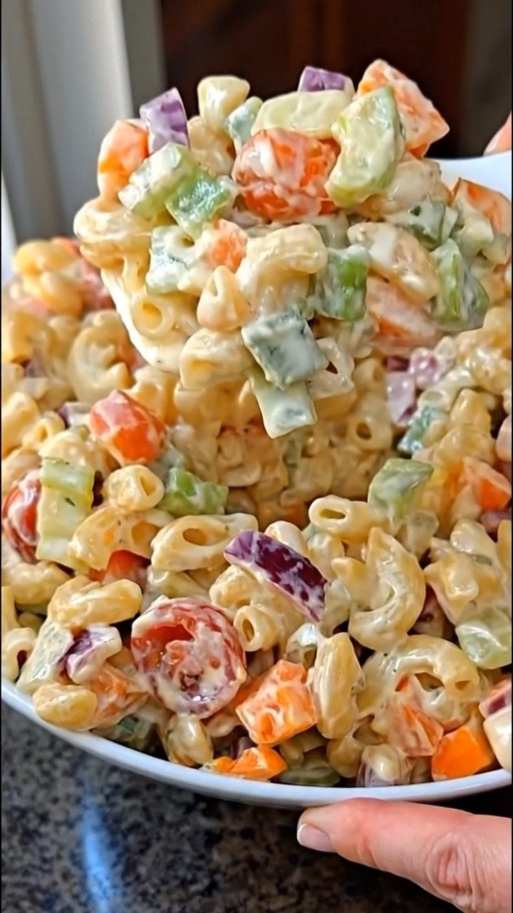 Macaroni pasta salad with carrots and celery in a white bowl.