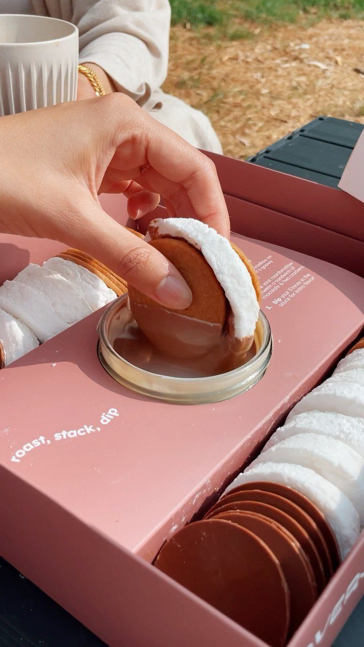 Hand dipping a s'more into a jar of melted chocolate in a pink kit.