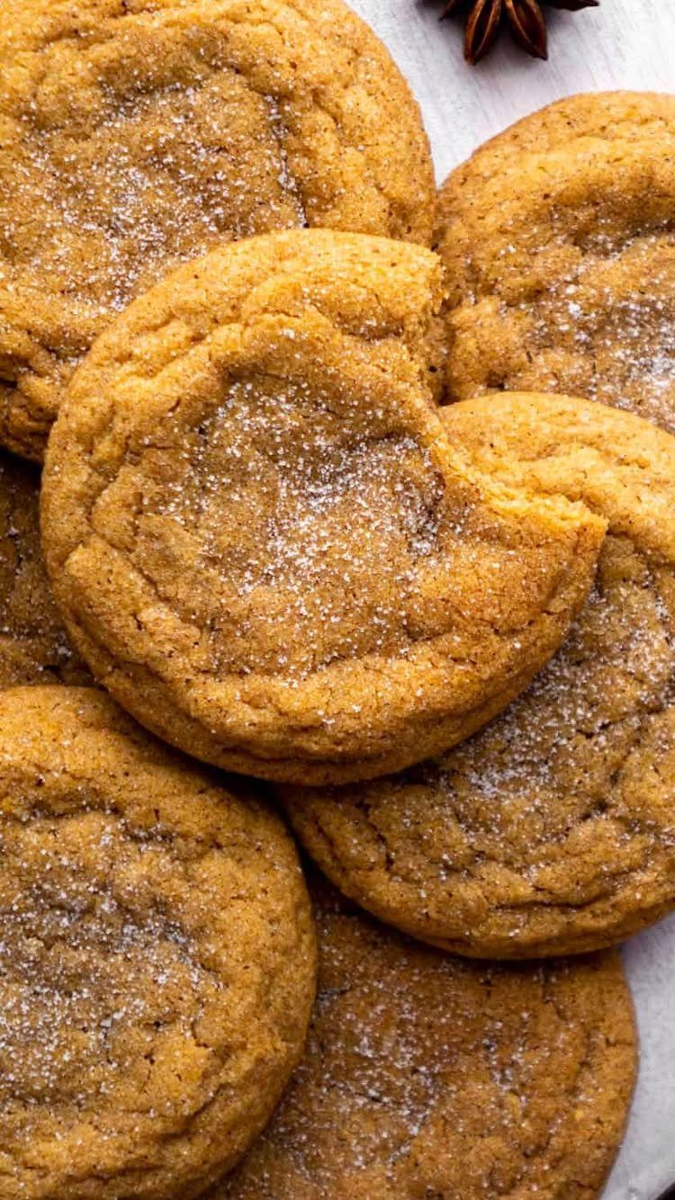 Sugar-dusted pumpkin spice cookies piled together with one cookie having a bite taken.