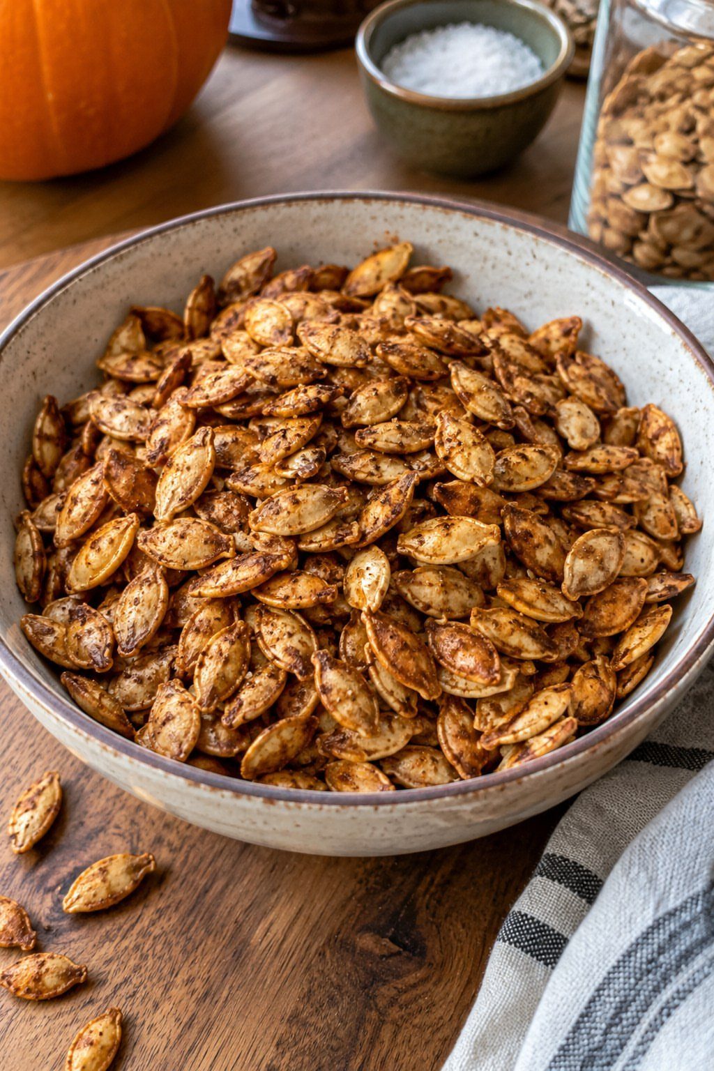 Roasted pumpkin seeds in a ceramic bowl on a wooden table with a pumpkin.