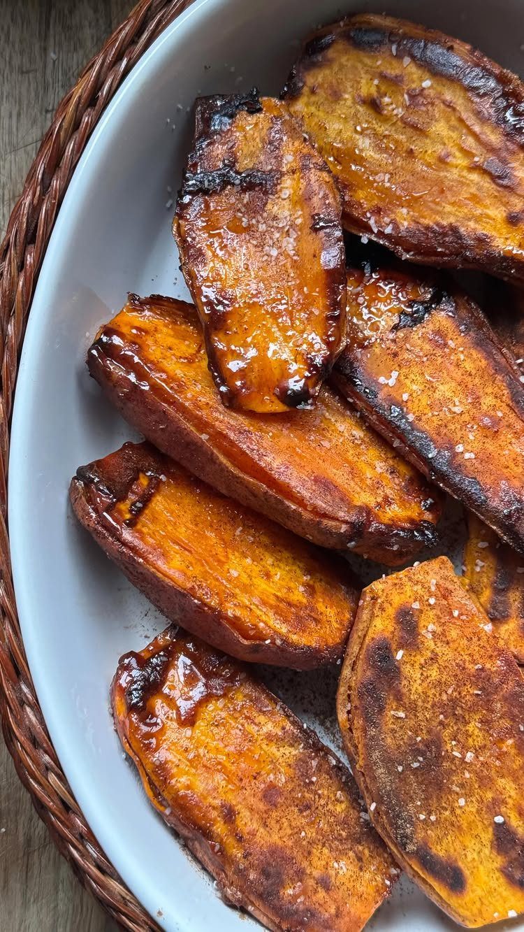 Roasted sweet potato wedges with charred edges on a white plate in a basket.