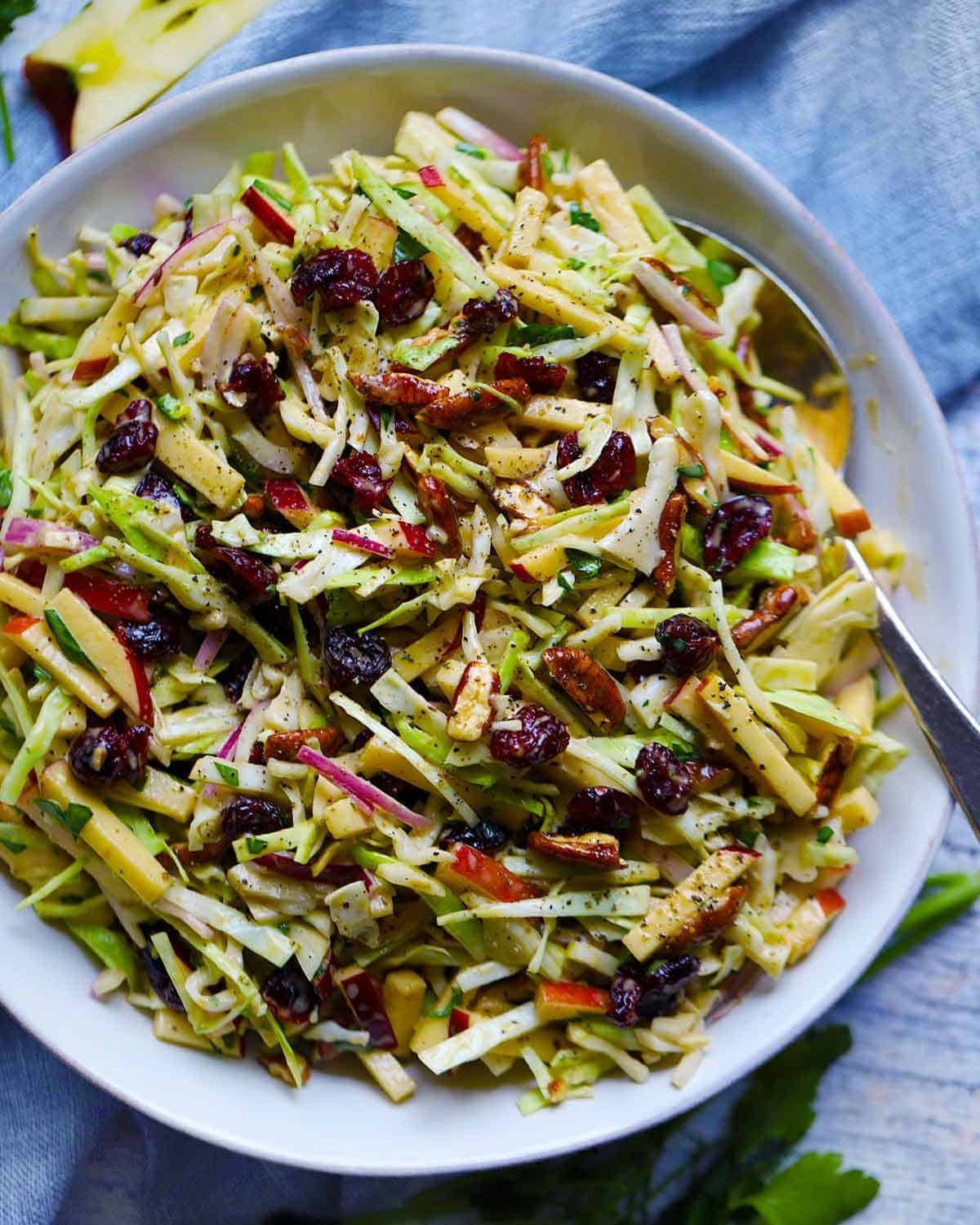 Colorful slaw with cabbage, dried cranberries, and nuts in a white bowl.